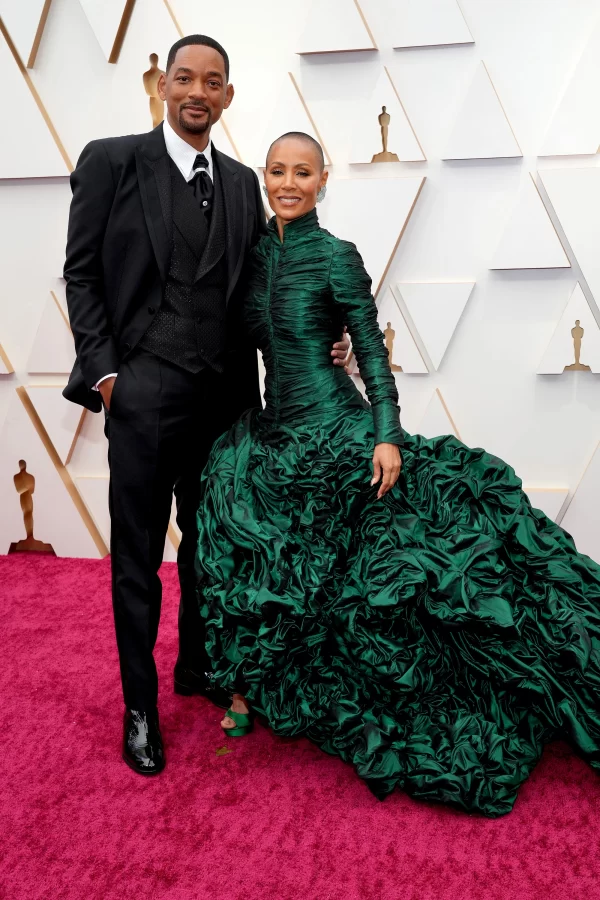 Jada Pinkett Smith poses in her green Dolce and Gabbana dress beside her husband Will at the Oscar Red Carpet ceremony before the awards show. Pinkett Smith has been open about her struggles with alopecia since she went public with her diagnosis in 2018, and is one of the top advocates for alopecia research. Chris Rock claims to have not known about Pinkett Smiths condition before making a joke at her expense.